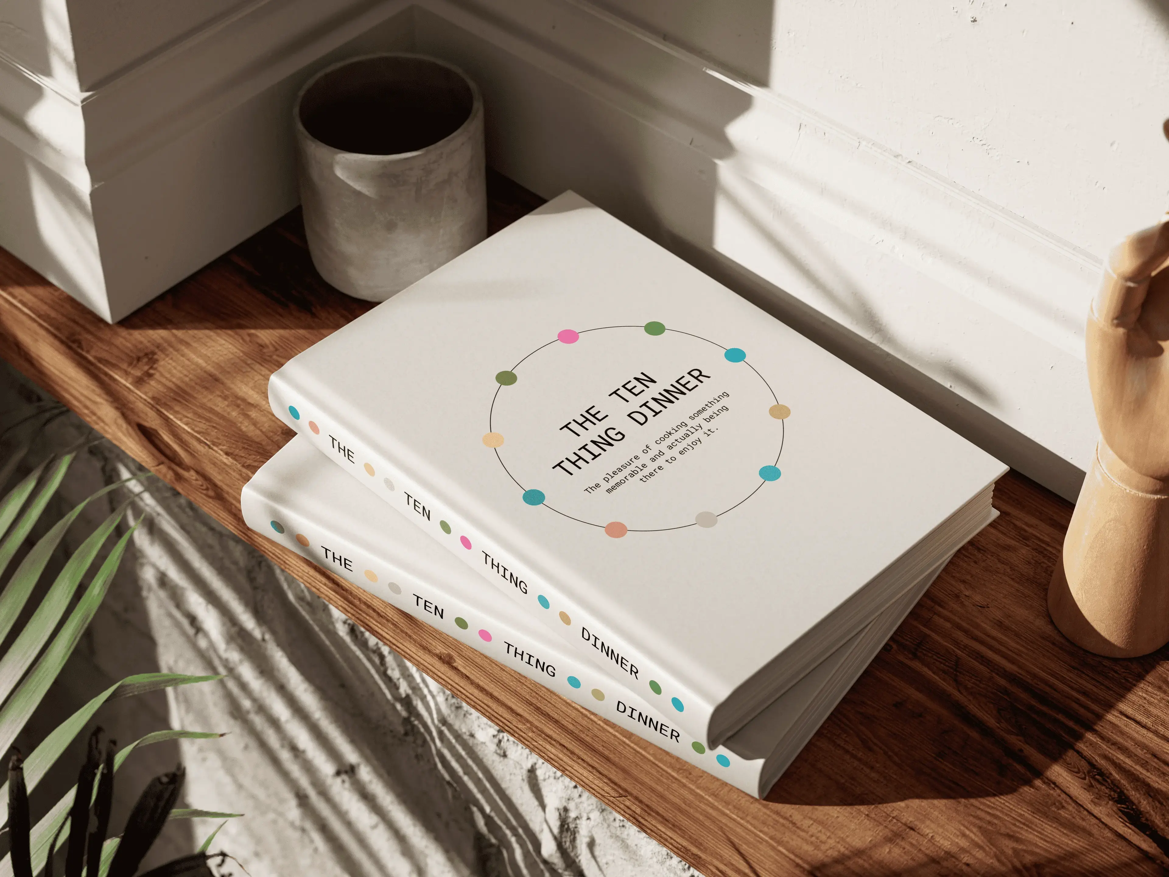 Two books titled "The Ten Thing Dinner" with colorful dots on the cover, placed on a wooden surface near a plant and a small pot.